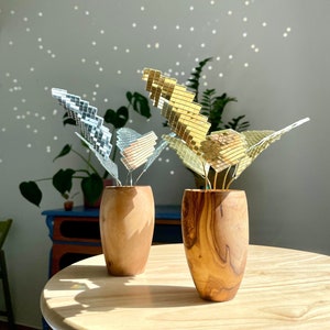 Könnte beinhalten: Zwei Holzvasen mit goldenen und silbernen Spiegelblättern. Die Vasen stehen auf einem Holztisch mit hellem Hintergrund.