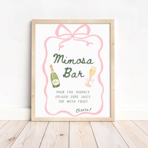 Puede incluir: Un letrero enmarcado con un marco de madera clara. El letrero tiene un lazo rosa en la parte superior y un borde rosa. Las palabras "Mimosa Bar" están en escritura verde. Debajo de las palabras hay instrucciones y la palabra "Cheers!"