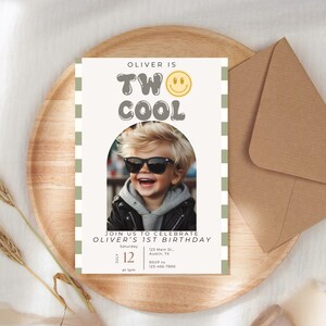 May include: A white invitation card with green and white checkered border. The card has a photo of a boy wearing sunglasses and a black leather jacket. The text on the card reads "Oliver is Two Cool" with a yellow smiley face. The invitation details include the date, time, and location of the event.