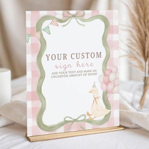 Peut inclure: Un panneau rectangulaire avec un fond vichy rose et blanc, une bordure en ruban vert sauge, une guirlande de fanions et un canard portant un chapeau de fête avec des ballons roses et blancs. Le texte indique : YOUR CUSTOM sign here ADD YOUR TEXT AND MAKE AN UNLIMITED AMOUNT OF SIGNS!