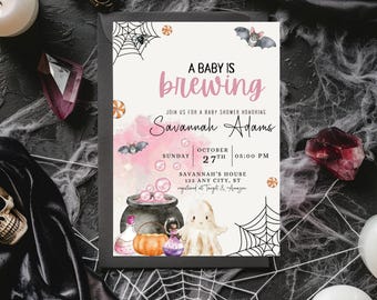 Op de afbeelding: Een baby shower uitnodiging met een roze en zwarte kleurstelling. De uitnodiging toont een ketel met borrelende drank, een pompoen, een spook en een vleermuis. De tekst luidt "A Baby is Brewing" en "Savannah Adams".
