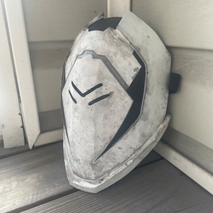 May include: A white and black plastic helmet with a textured surface and a black strap. The helmet has a geometric design with a black and white pattern.