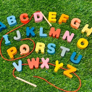 May include: A colorful wooden alphabet set with letters A through Z, each in a different color, strung on a red cord. The letters are arranged on a bed of green grass, perfect for early learning and educational play.