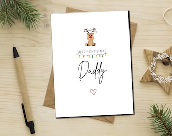 Op de afbeelding: Een witte kerstkaart met een cartoon rendier met een rode neus en gewei. De kaart zegt "Merry Christmas Daddy" met een reeks gekleurde lampjes en een rood hart.
