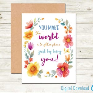 May include: A greeting card with a floral wreath design. The card features the text "YOU MAKE the world a brighter place just by being you!" in various colors. A brown envelope is behind the card.