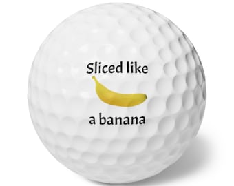 May include: White golf ball with the text "Sliced like a banana" and a yellow banana graphic. The golf ball has a dimpled surface.