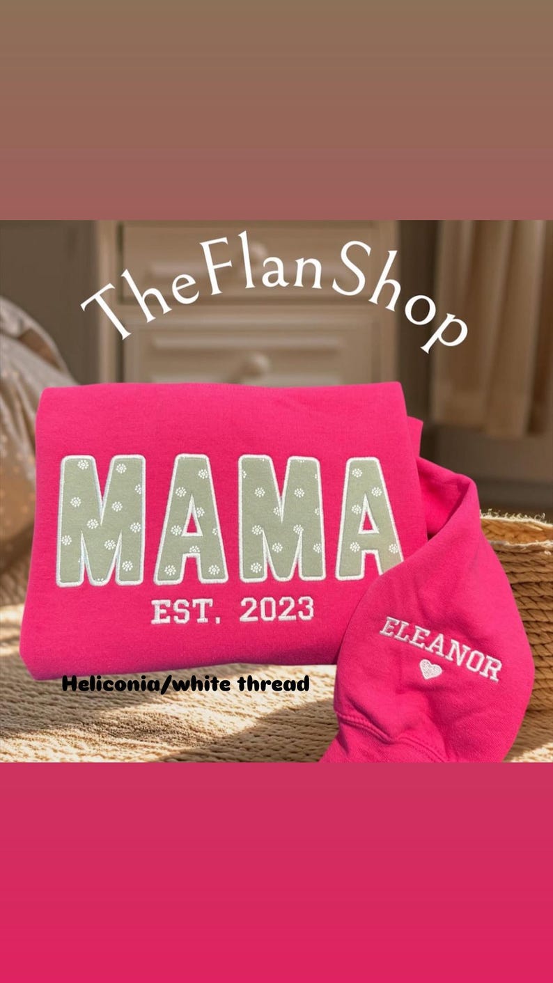 K&ouml;nnte beinhalten: Rosafarbener Pullover mit dem Text "MAMA EST. 2023" in wei&szlig;er Schrift auf der Vorderseite und "ELEANOR" mit einem Herz in wei&szlig;er Schrift auf dem &Auml;rmel. Der Pullover ist aus Heliconia-Stoff gefertigt.