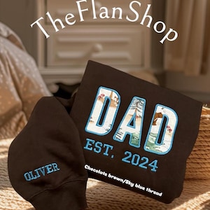 K&ouml;nnte beinhalten: Zwei schwarze Kapuzenpullover mit gesticktem Text. Ein Pullover sagt "DAD EST. 2024" mit einer Waldszene in den Buchstaben. Der andere Pullover sagt "OLIVER". Der Text ist in Himmelblau und Schokoladenbraun gestickt.