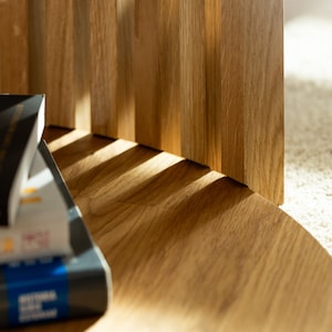 May include: Close-up of a wooden table with a rounded edge. The table is made of light brown wood with a natural grain pattern. A stack of books is sitting on the table.