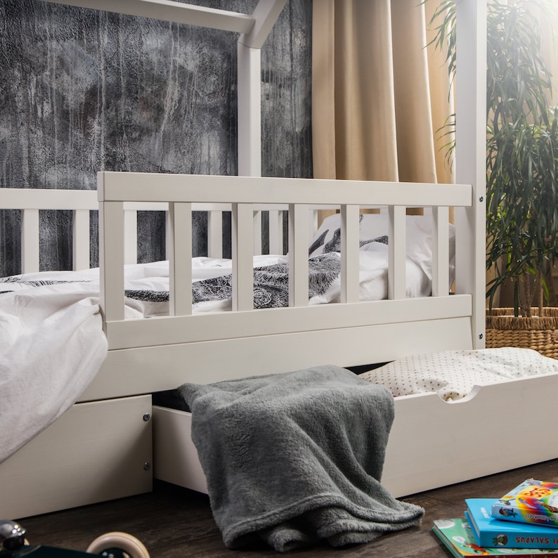 Peut inclure: Lit d'enfant en bois blanc avec un matelas blanc et un tiroir blanc en dessous. Le lit est dot&eacute; d'une barri&egrave;re en bois blanc autour du matelas.