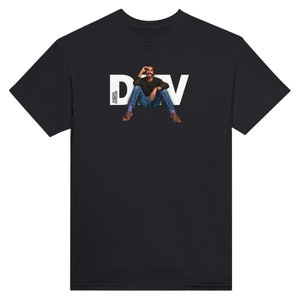 Op de afbeelding: Zwart T-shirt met een witte afbeelding van een man die zit met de tekst "DAV" erboven.