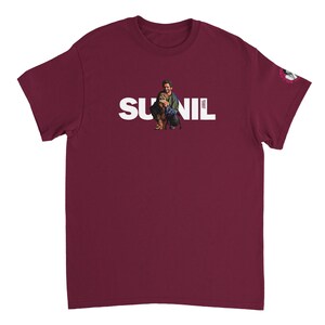 May include: Burgundy t-shirt with the name "SUNIL" in white block letters. A graphic of a person and a dog is centered above the name. The sleeve has a small graphic. The shirt is made of a soft material.