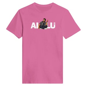 May include: Pink t-shirt with a white graphic of a man sitting with the text "AI LU" above him.