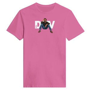 Può includere: Maglietta rosa con una grafica bianca di un uomo seduto con il testo "DAV" sopra di lui.