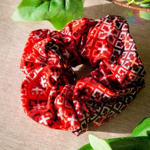 Könnte beinhalten: Ein roter und schwarzer Scrunchie mit geometrischem Muster. Der Scrunchie ist aus weichem, dehnbarem Stoff und hat einen dezenten Schimmer.