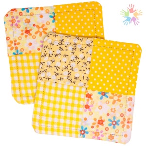 Könnte beinhalten: Zwei quadratische Stoffuntersetzer mit Patchwork-Design. Jeder Untersetzer hat eine Kombination aus gelben Stoffen mit Blumen-, Tupfen- und Vichy-Mustern. Die Kanten sind sauber mit gelbem Faden genäht.