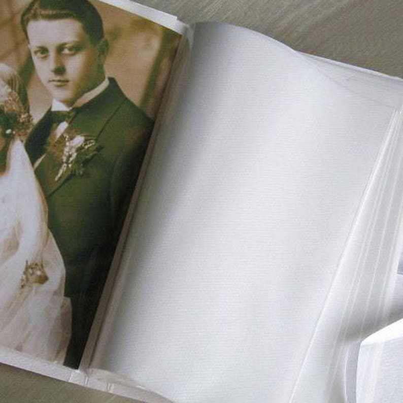 May include: A vintage photo album with a white cover and a photo of a couple on the front. The photo shows a man in a suit and a woman in a white dress.