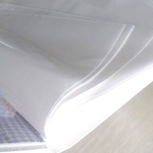 May include: A clear plastic sheet protector with a textured surface. The sheet protector is folded in half and is lying on a white surface.