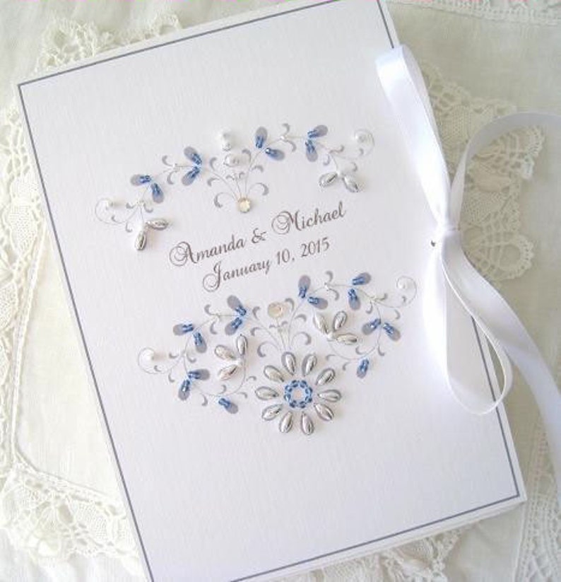 May include: A white wedding guest book with a blue and silver floral design and the text "Amanda & Michael January 10, 2015".