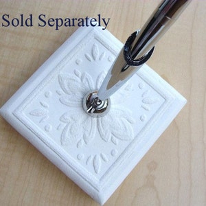 K&ouml;nnte beinhalten: Wei&szlig;er Keramik-Stiftst&auml;nder mit einem dekorativen Blumenmuster. Der St&auml;nder hat eine silberne Metallbasis und ist f&uuml;r die Aufnahme eines Stifts oder Bleistifts konzipiert.