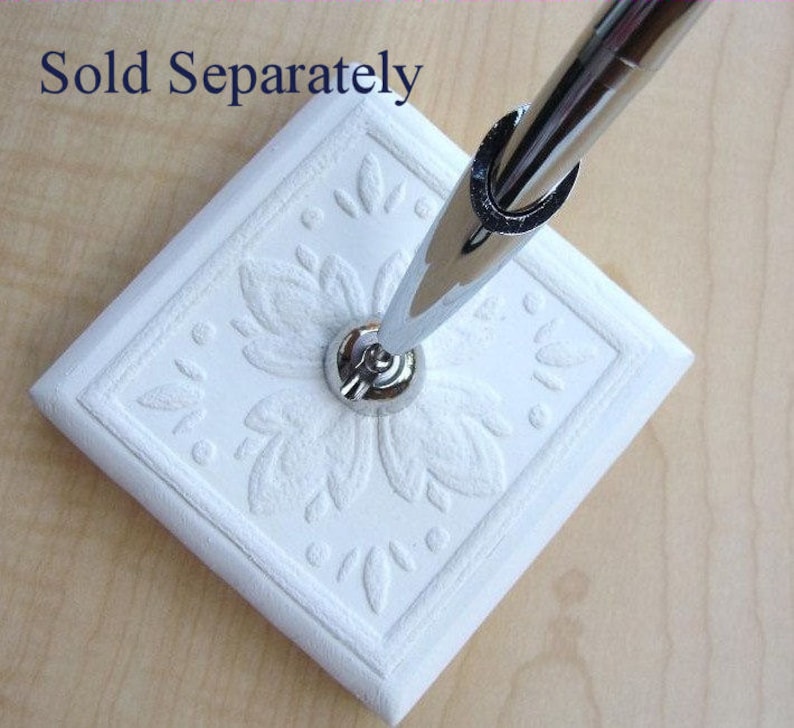 K&ouml;nnte beinhalten: Wei&szlig;er Keramik-Stiftst&auml;nder mit einem dekorativen Blumenmuster. Der St&auml;nder hat eine silberne Metallbasis und ist f&uuml;r die Aufnahme eines Stifts oder Bleistifts konzipiert.