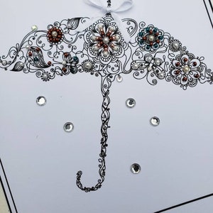 May include: A white card with a black and white illustration of an umbrella with a white bow. The umbrella is decorated with pearls and rhinestones. The card has the text "Ansley's Shower 1th 2021" at the bottom.