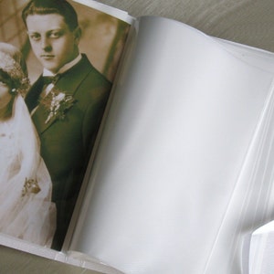 May include: A vintage wedding photo album with a sepia-toned photo of a bride and groom on the front cover. The album is open to a blank page.
