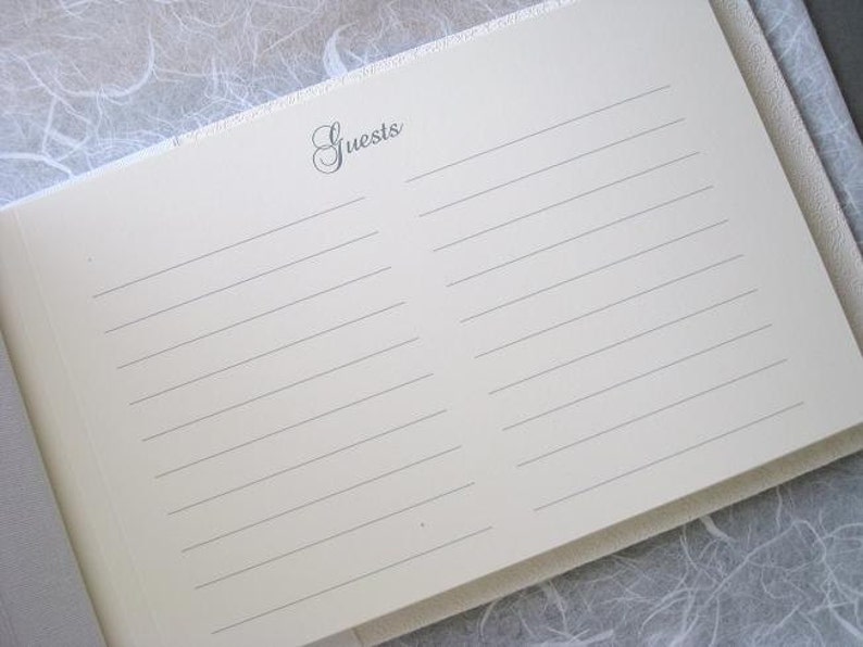 K&ouml;nnte beinhalten: Ein wei&szlig;es G&auml;stebuch mit einem schlichten, eleganten Design. Der Einband hat eine dezente Textur und das Wort "Guests" ist in einer kursivschriftlichen Schriftart gedruckt.