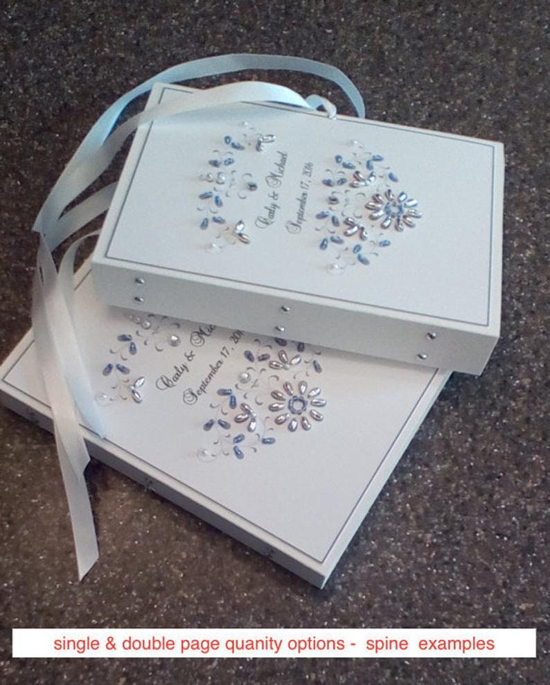 May include: Two white wedding guest books with blue and silver embellishments. The top book has the text "Carly & Michael September 17, 2018".