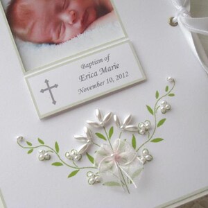 May include: A white card with a green floral design and white pearl accents. The card has a photo of a baby and a text box that reads "Baptism of Erica Marie November 10, 2012".
