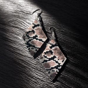 Peut inclure: Une paire de boucles d'oreilles en forme de losange avec un motif peau de serpent. Les boucles d'oreilles présentent une combinaison de perles roses, noires, blanches et grises. Les boucles sont suspendues à des crochets argentés.