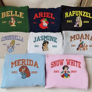 May include: A selection of sweatshirts in different colours, each displaying a princess name in arched lettering. Each sweatshirt has a princess illustration and the year the princess was established.