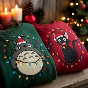 Puede incluir: Dos sudaderas navideñas. Una es verde bosque con un personaje de dibujos animados con gorro de Papá Noel, rodeado de luces de colores. La otra es roja, con un gato negro con gorro de Papá Noel, también con luces. Ropa festiva navideña.