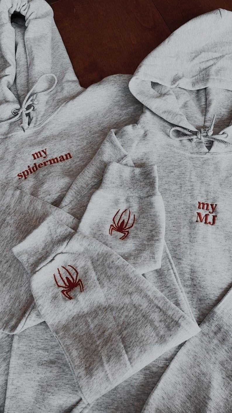 Puede incluir: Dos sudaderas con capucha grises con dise&ntilde;os de ara&ntilde;as bordadas en rojo y texto. Una sudadera dice "my spiderman" y la otra dice "my MJ".