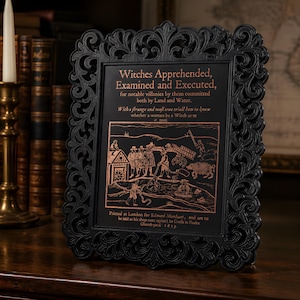May include: A black ornate picture frame containing a print with copper-colored text and a historical illustration. The text reads: Witches Apprehended, Examined and Executed, for notable villanies by them committed both by Land and Water.
