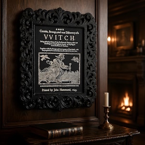 May include: A black framed wall art piece featuring a white text reproduction of a 1643 pamphlet titled A Most Certain, Strange, and true Discovery of a VVITCH, with an illustration of a figure on a plank board and printed by John Hammond.