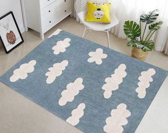 May include: A blue rug with a cloud pattern in white. The rug is rectangular and placed on a light-colored floor. The room also features a white dresser, a framed picture, a chair with a yellow pillow, and a potted plant.