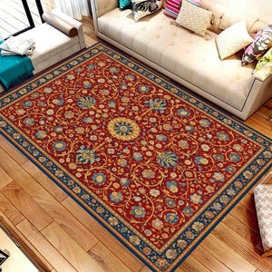 Puede incluir: Una alfombra rectangular con un intrincado diseño floral. La alfombra presenta un fondo rojo intenso, un medallón central y un borde azul marino. El diseño floral incluye tonos dorados, azules y crema.