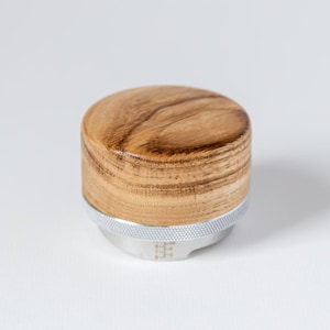 Puede incluir: Un tamper de madera para un molinillo de café, con una base plateada y una parte superior de madera. La madera tiene un patrón de veta natural.