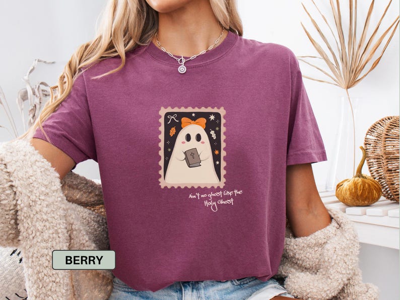 K&ouml;nnte beinhalten: Beerenfarbenes T-Shirt mit einem stempelartigen Aufdruck eines Geistes, der ein Buch und eine orangefarbene Schleife h&auml;lt. Der Text auf der Grafik lautet "Ain't no ghost like the Holy Ghost". Es ist ein Freizeitkleidungsst&uuml;ck.