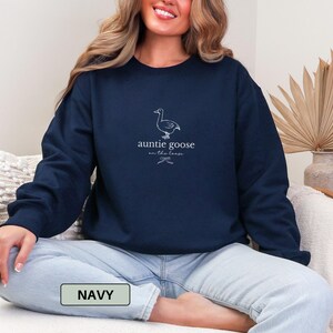 Może przedstawiać: Granatowa bluza z napisem "auntie goose on the loose" i ilustracją gęsi. Bluza jest w jednolitym granatowym kolorze. Słowo "NAVY" znajduje się w prostokącie na dole obrazu.