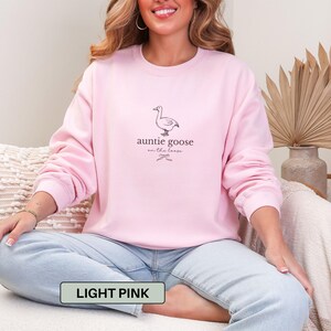 Może przedstawiać: Jasnor&oacute;żowa bluza z napisem "auntie goose on the loose" i ilustracją gęsi. Tekst "light pink" znajduje się w prostokącie na dole obrazu. Bluza jest w kolorze jasnor&oacute;żowym.