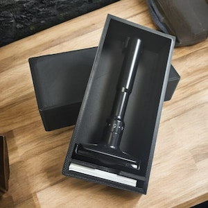 May include: A black safety razor with a numbered dial and a black case. The razor is in the case, with the handle sticking out.