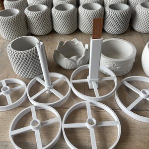 Puede incluir: Un surtido de macetas y accesorios de cerámica blanca. Las macetas tienen un diseño geométrico de celosía. Otros artículos incluyen un plato en forma de loto, un plato redondo con un borde decorativo y ruedas blancas con un cubo central.