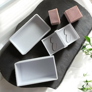 Op de afbeelding: Een set van drie keramische mokken met een gespikkelde, matte afwerking. De mokken zijn in crème, lichtgrijs en donkergrijs. Elke mok heeft een eenvoudig, minimalistisch ontwerp.