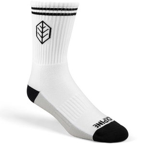 Puede incluir: Calcetines blancos de caña alta con rayas negras y un logotipo negro en la parte delantera. El logotipo es una hoja estilizada dentro de un hexágono. Los calcetines tienen un talón y una puntera negros.