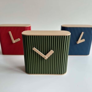 Puede incluir: Tres relojes pequeños cuadrados con un diseño acanalado. Los relojes son de color rojo, verde y azul. Cada reloj tiene una manecilla de hora y minuto de madera simple.