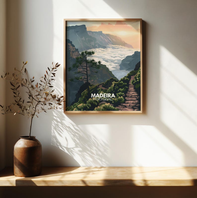 May include: A vintage travel poster with a scenic view of a mountain path leading to a valley with clouds. The poster is framed in wood and has the text "MADEIRA PORTUGAL" at the bottom.