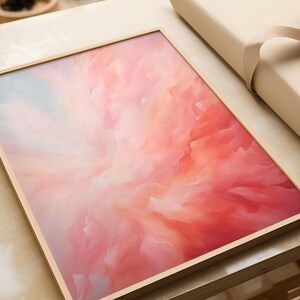 Peut inclure: Une œuvre d'art murale encadrée rectangulaire présentant une composition abstraite de teintes roses, corail et blanc doux mélangées. Le motif affiche des formes fluides semblables à des nuages rayonnant du centre, dans un cadre en bois clair.