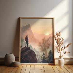 K&ouml;nnte beinhalten: Ein gerahmter Druck eines Wanderers, der auf einer felsigen Klippe steht und auf ein nebliges Bergtal bei Sonnenaufgang blickt. Der Wanderer tr&auml;gt einen Rucksack und schaut auf die Aussicht.